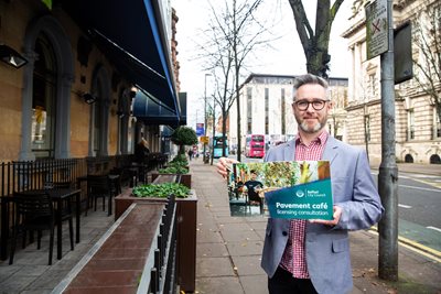 Councillor Gary McKeown holds a poster promoting the pavement café licensing scheme consultation - on a pavement in the city centre.