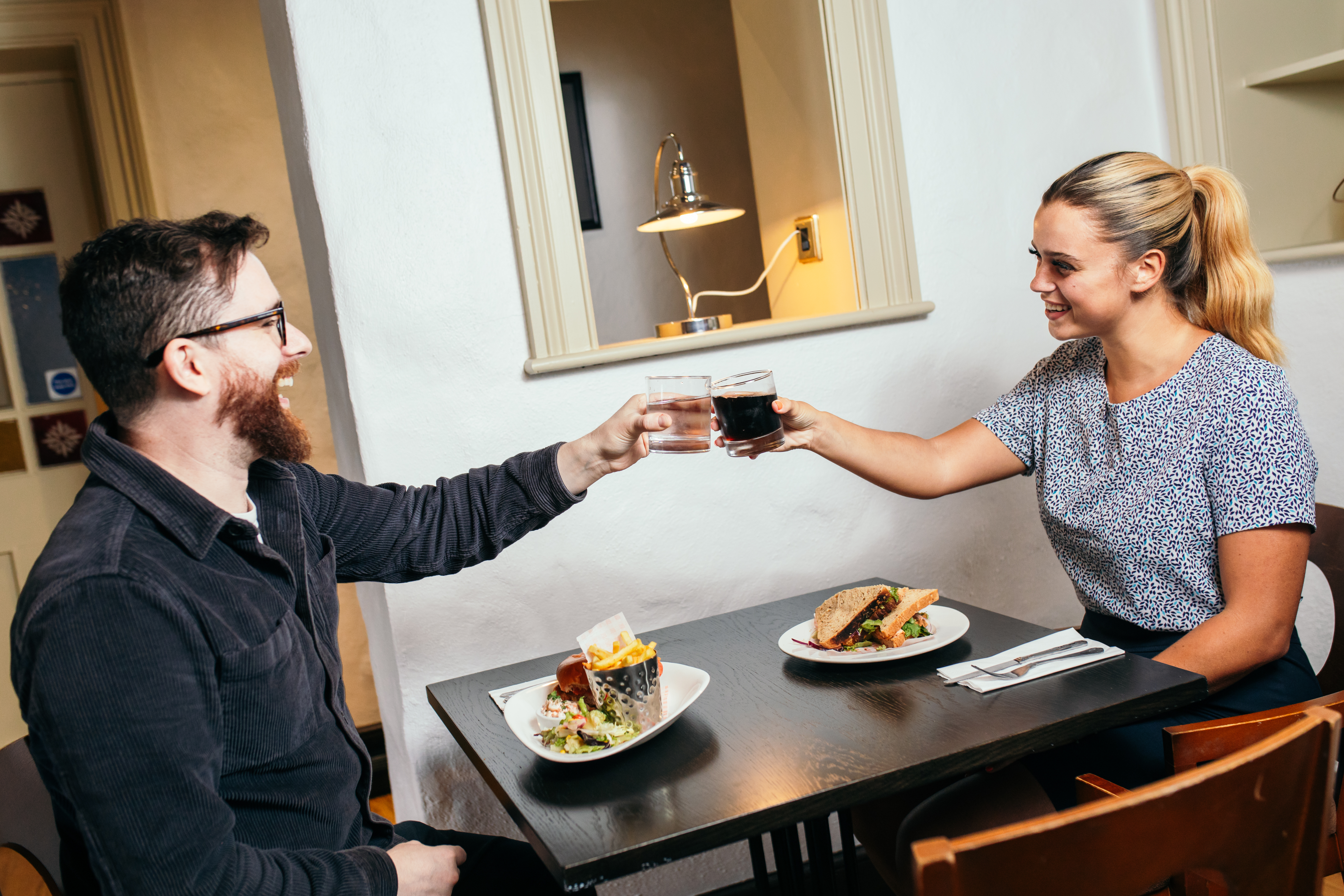 A man and woman sitting inside at a table enjoying drinks and lunch.
